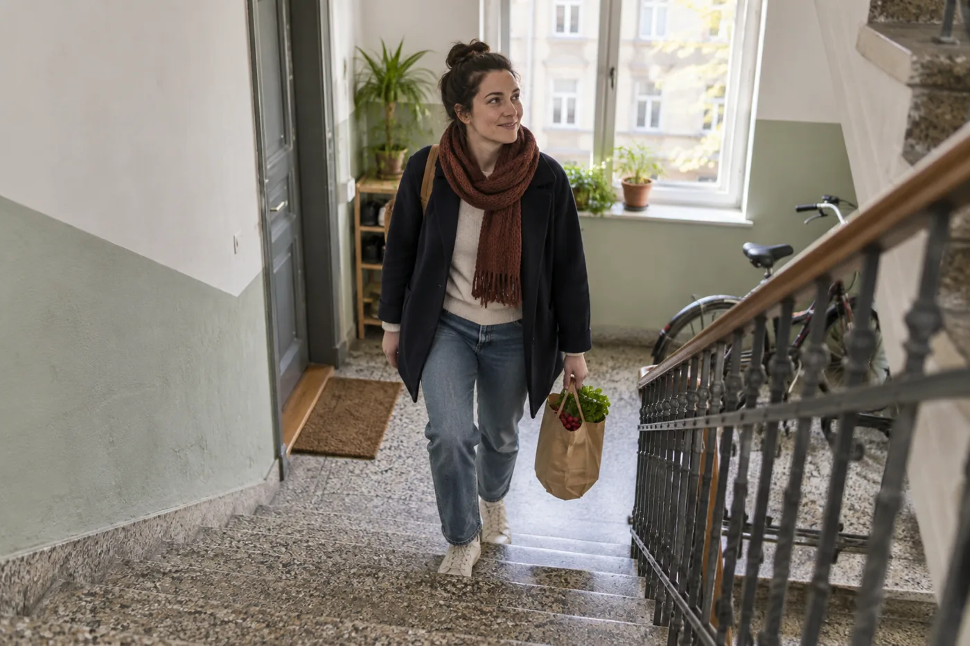 Frau trägt einen Einkauf eine Treppe im Wohnhaus hinauf